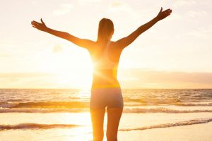 Frau am Strand voller Lebensfreude breitet die Arme aus.